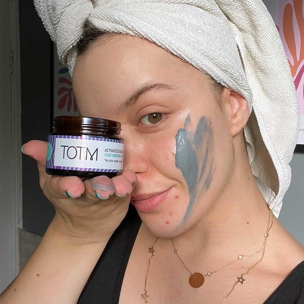 Girl holding TOTM face mask with the charcoal mask smudged onto cheek