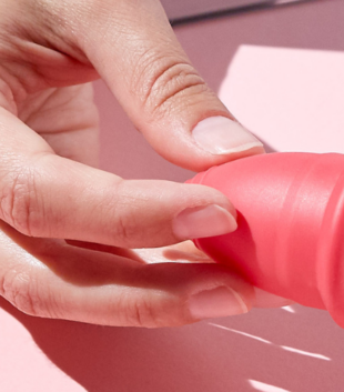 A hand holding menstrual cup on pink background