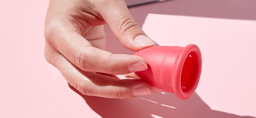 A hand holding menstrual cup on pink background