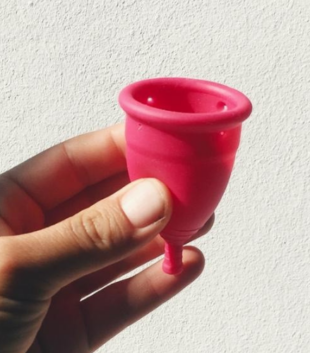 Hand holding pink menstrual cup against a white wall with a shadow effect. An example of one of the many sustainable period products.