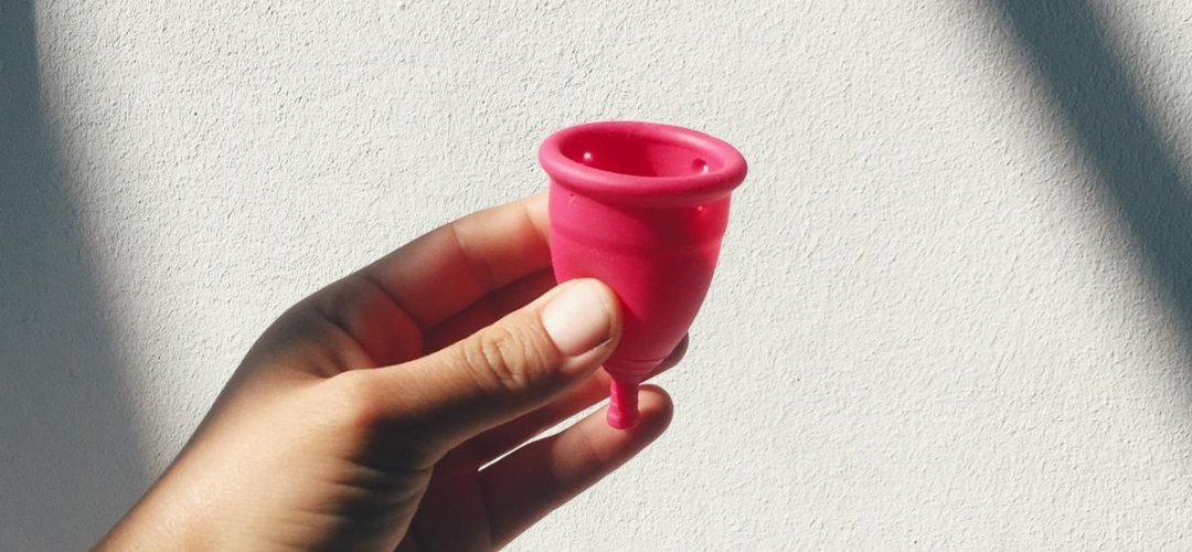 Hand holding pink menstrual cup against a white wall with a shadow effect. An example of one of the many sustainable period products.