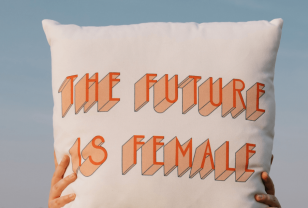 Hands holding up a cushion with the future is female in orange text on it against blue sky background