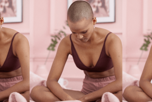 Female PoC is sitting cross-legged in a pink bedroom looking down in her lap