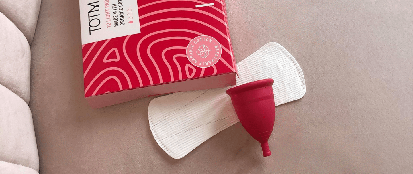 TOTM's reusable zero-waste menstrual cup, organic cotton liner and organic cotton light flow pads box on pink background