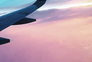 Plane wing flying through pink sunset sky