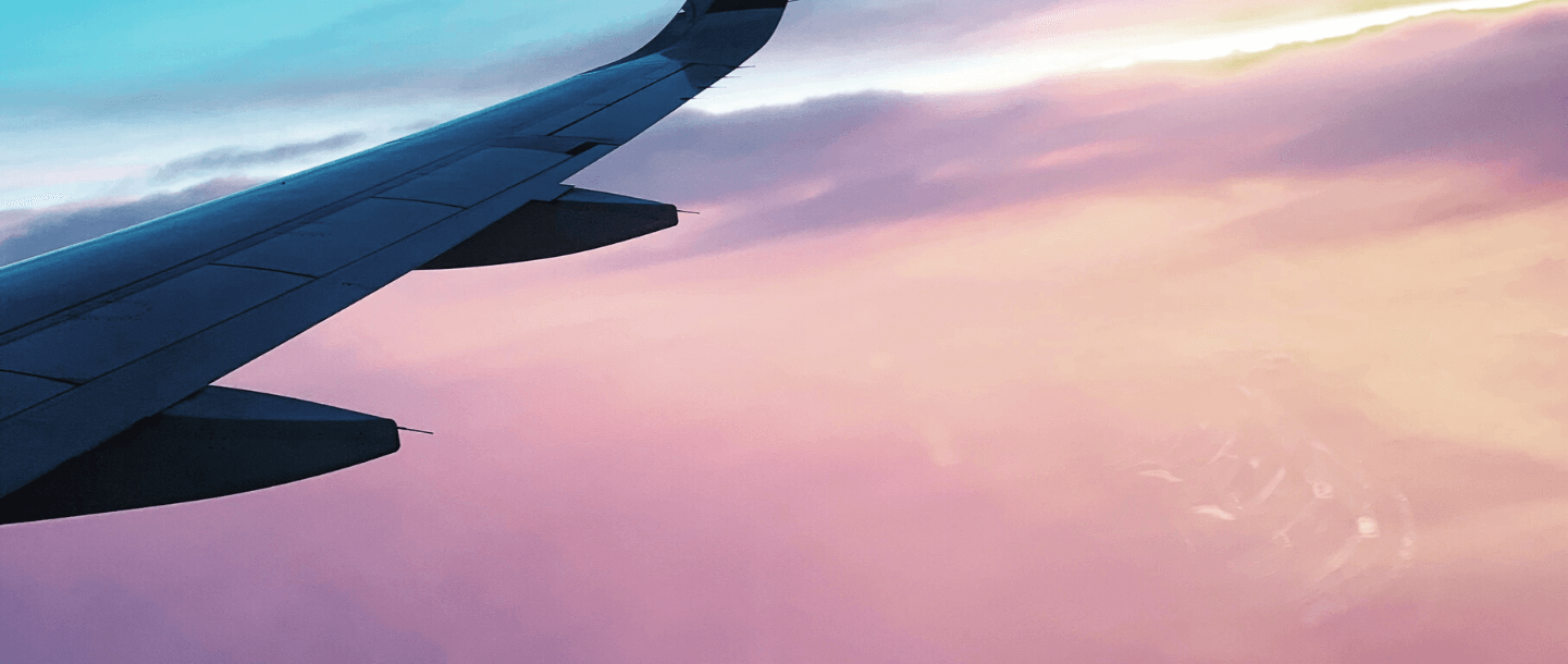 Plane wing flying through pink sunset sky