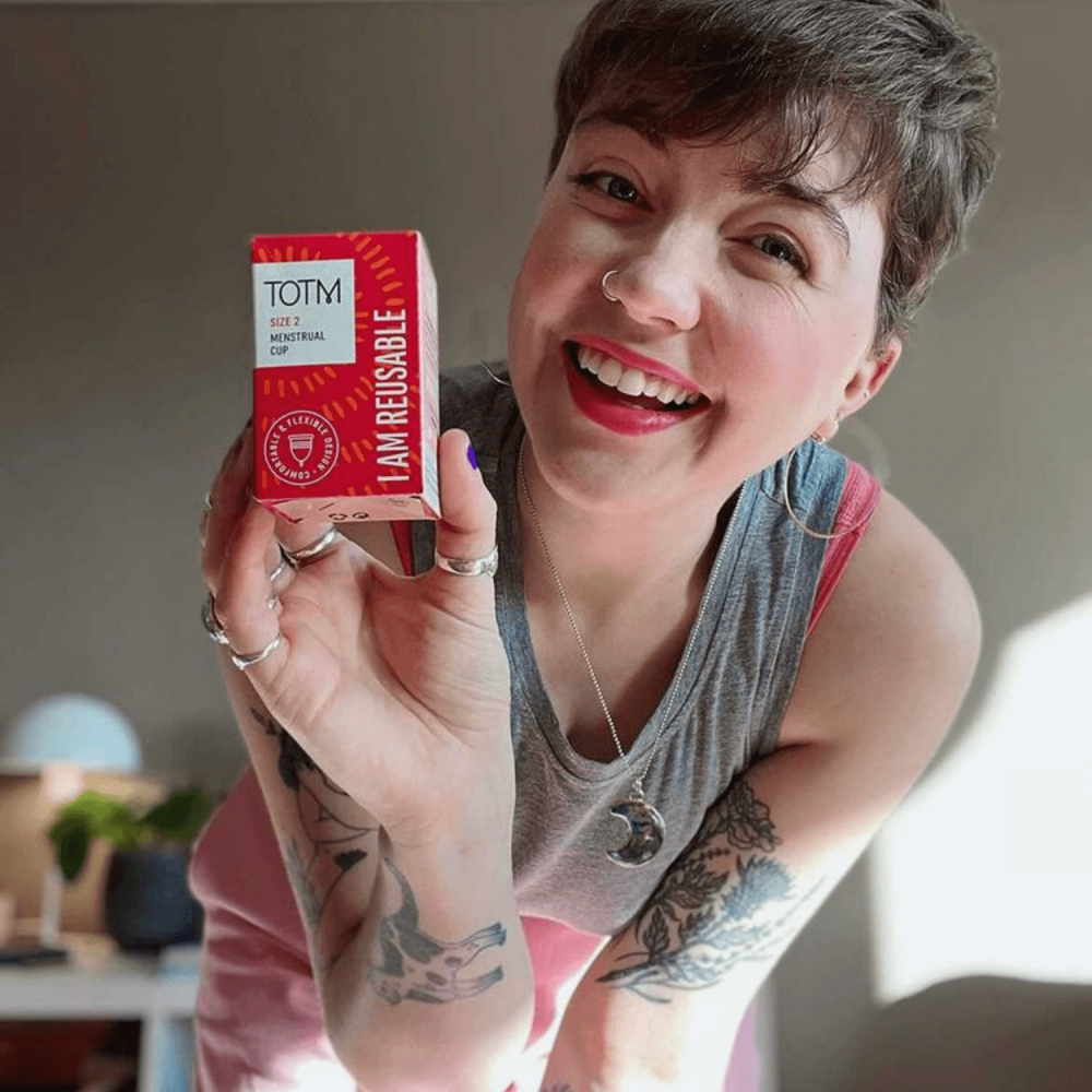 Female smiling and holding TOTM menstrual cup box in bedroom