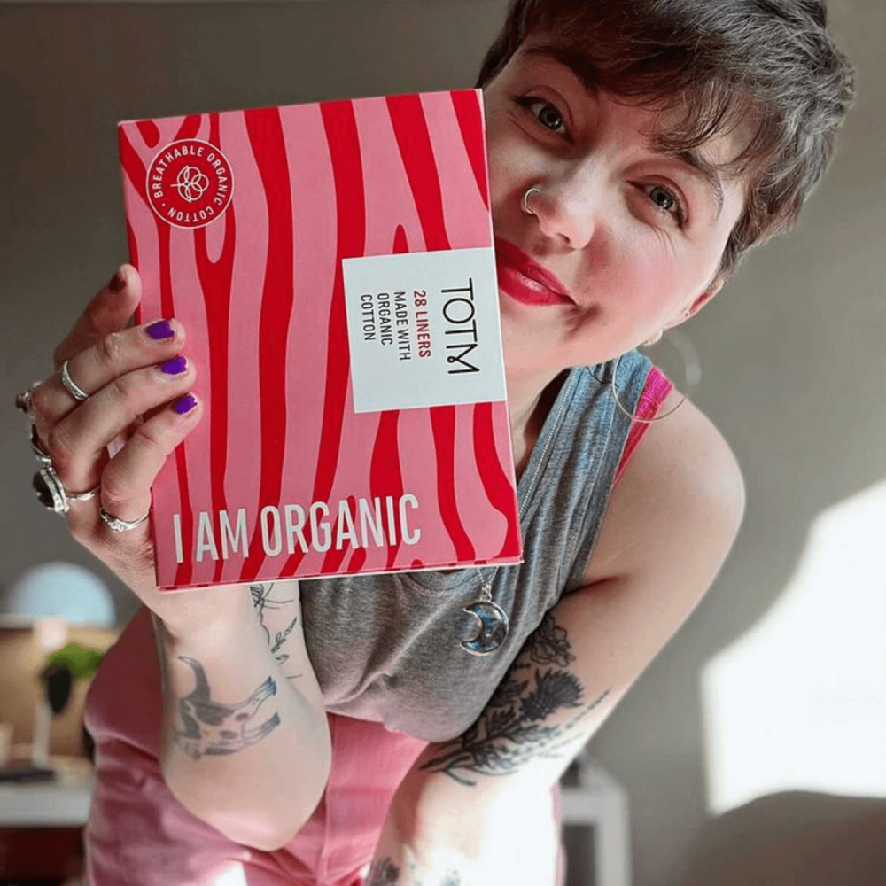 Female smiling to camera holding light pink and bright pink TOTM liners box