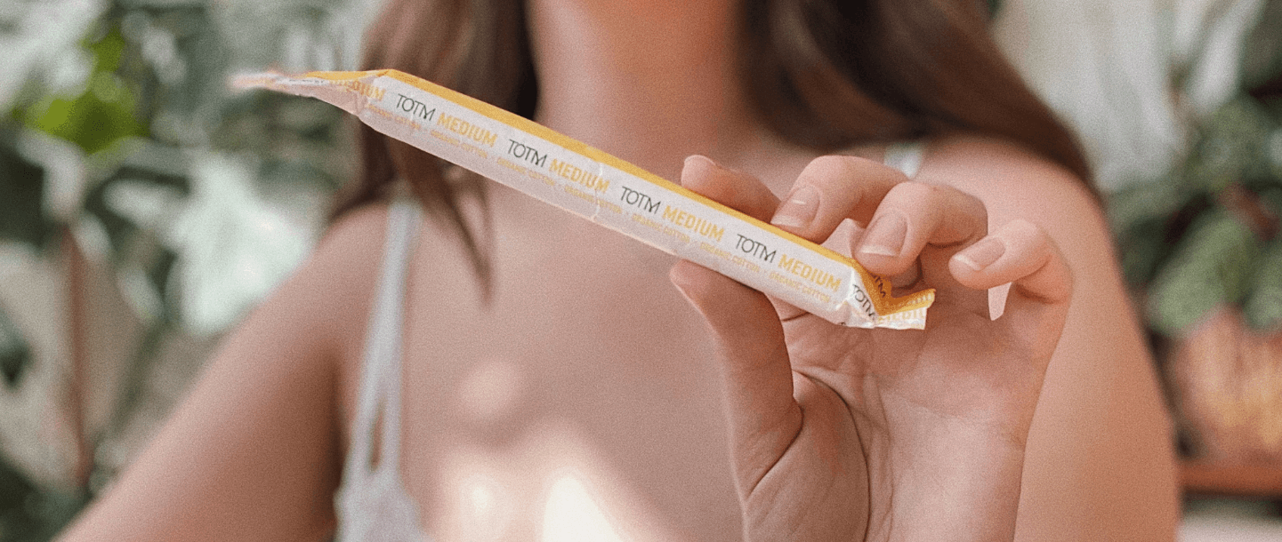 Close-up of TOTM's organic cotton medium cardboard applicator tampon wrapper in the hand of a young white female