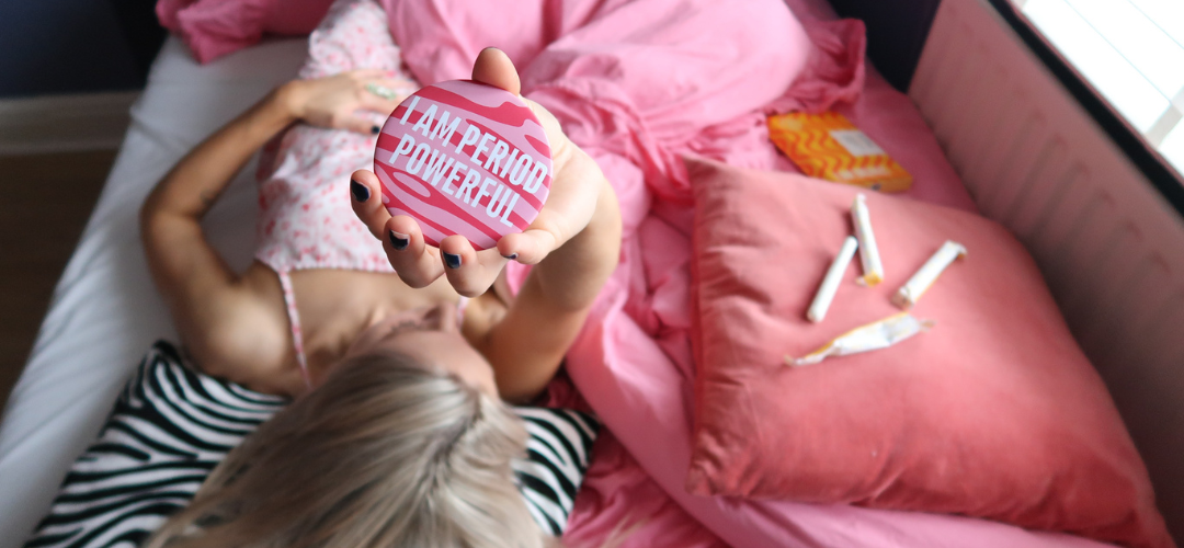 Woman holding period powerful pink mirror with tampons next to her on pillow