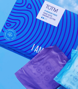 TOTM's medium flow organic cotton pads box next to medium and super pad in their wrapper on a blue background with sky reflection