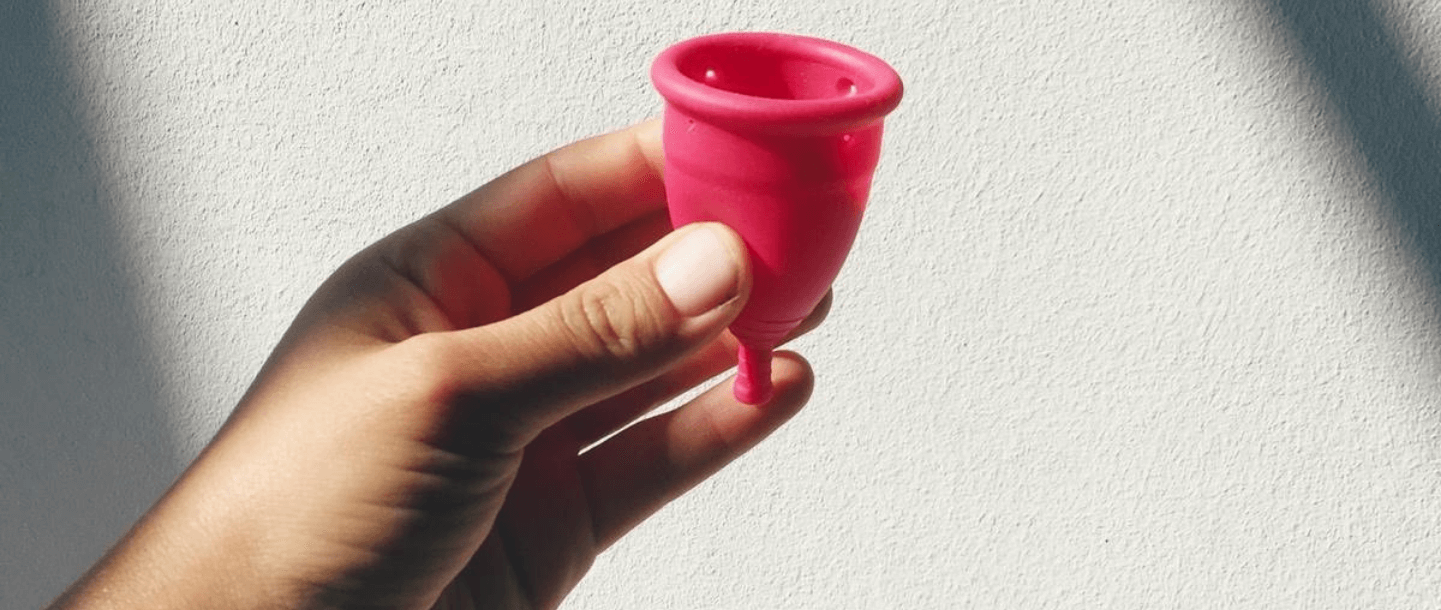 Close-up of a hand holding a TOTM reusable zero-waste menstrual cup against a white background