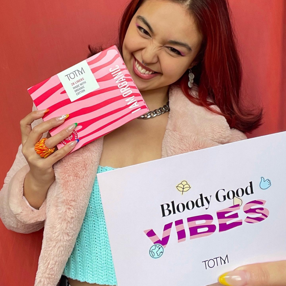 Girl on a red background smiling holding TOTM liners and a discount code flyer from the brand