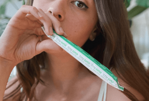 Close-up of a brunette female holding a TOTM organic cotton cardboard applicator super tampon in wrapper with her hand over her mouth