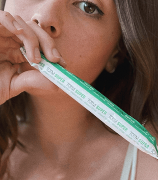 Close-up of a brunette female holding a TOTM organic cotton cardboard applicator super tampon in wrapper with her hand over her mouth