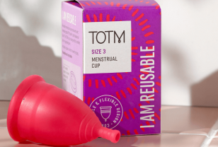 TOTM's size 3 menstrual cup unboxed and lying beside the packaging box on top of pink tiles