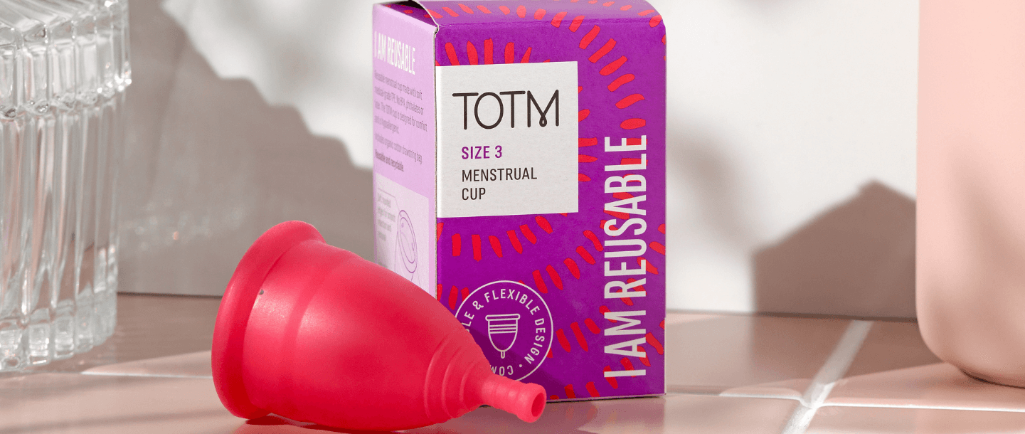 TOTM's size 3 menstrual cup unboxed and lying beside the packaging box on top of pink tiles