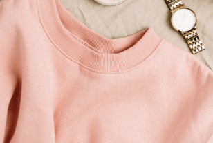 top half of a peach coloured sweatshirt on beige fabric background next to a watch and makeup