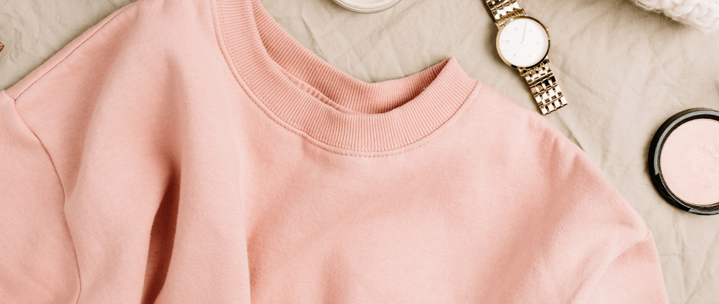 top half of a peach coloured sweatshirt on beige fabric background next to a watch and makeup